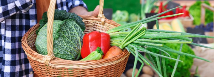 Photo of Man with different vegetables in wicker basket at farmer's market, closeup