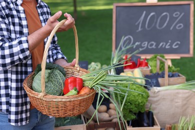 Photo of Man with different vegetables in wicker basket at farmer's market, closeup