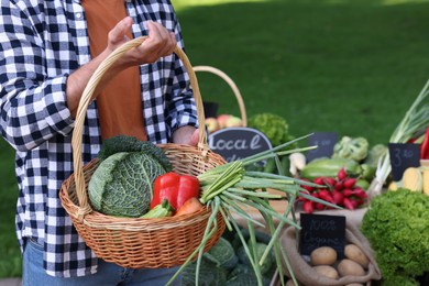 Photo of Man with different vegetables in wicker basket at farmer's market, closeup