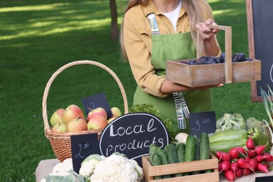 Photo of Farmer with basket of plums near stall with different fresh vegetables at market, closeup