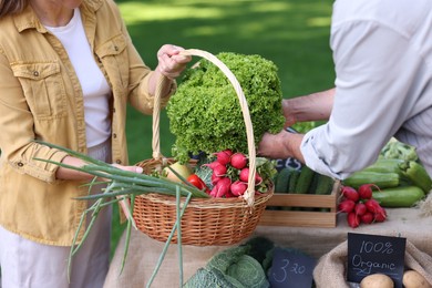 Photo of Woman choosing fresh vegetables from stall at farmer's market, closeup