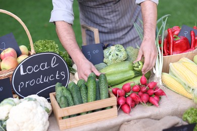 Photo of Farmer near stall with different fresh vegetables at market, closeup