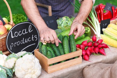 Photo of Farmer near stall with different fresh vegetables at market, closeup