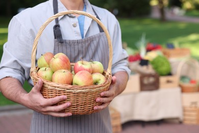 Photo of Farmer with apples in wicker basket near stall market, closeup