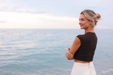 Photo of Beautiful young woman near sea on beach, space for text