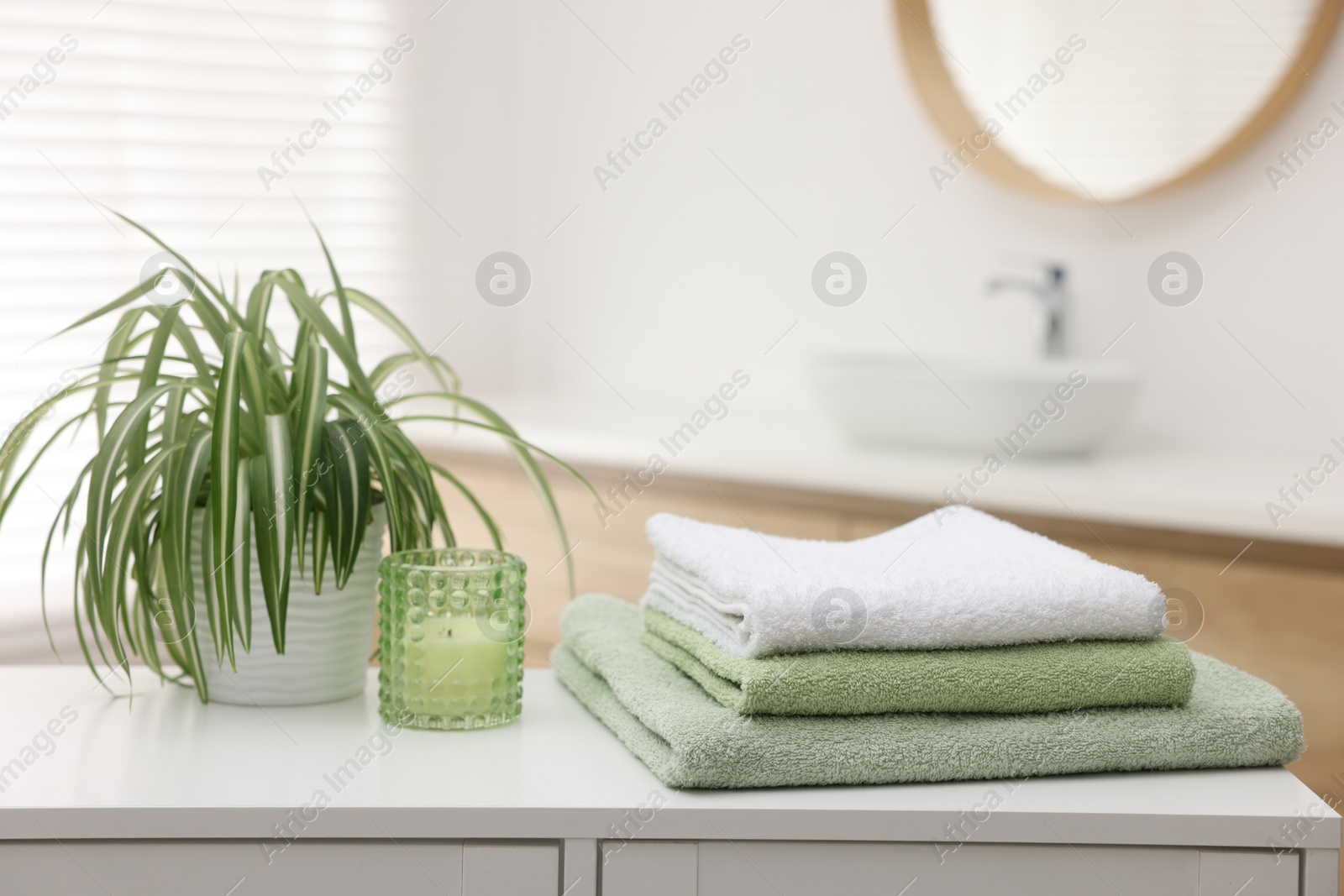 Photo of Stack of fresh terry towels, candle and plant on white table in bathroom. Space for text