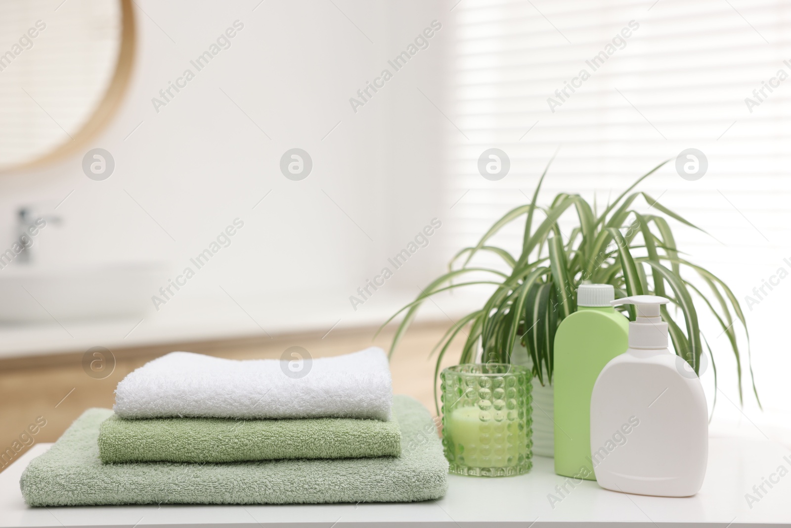 Photo of Stack of fresh terry towels, cosmetic products, candle and plant on white table in bathroom. Space for text
