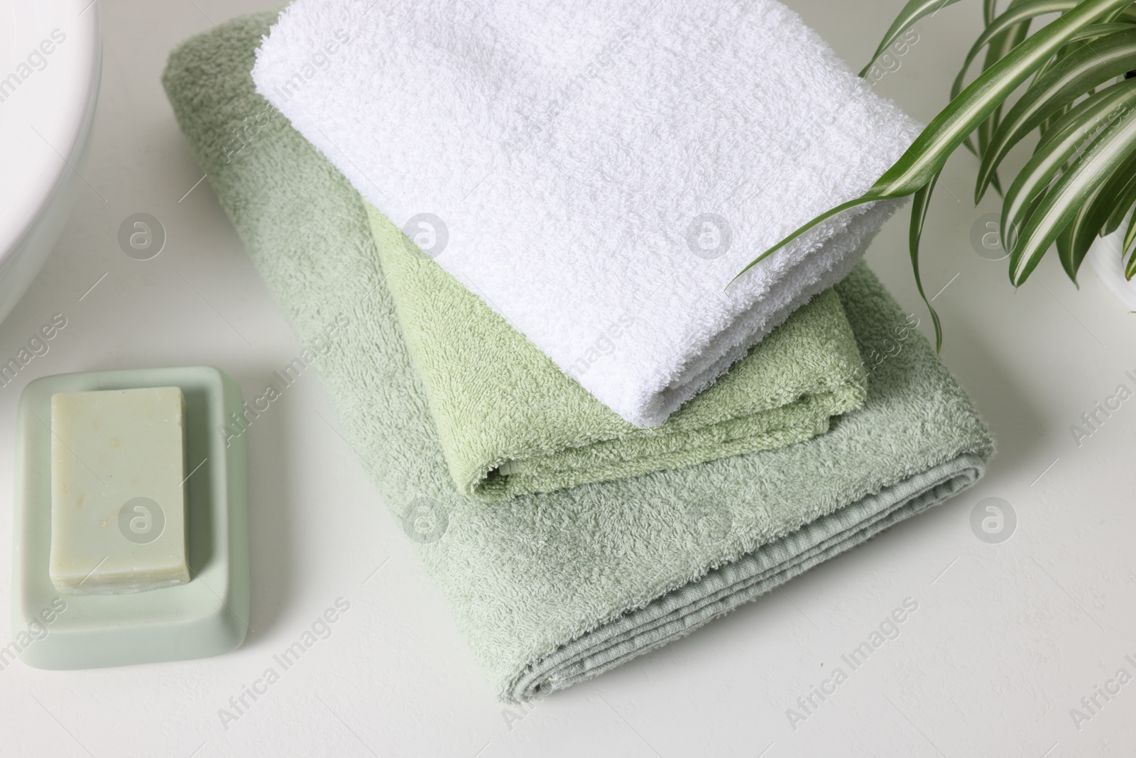 Photo of Stack of fresh terry towels and soap on white table, closeup