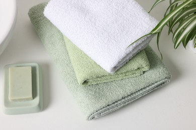 Photo of Stack of fresh terry towels and soap on white table, closeup