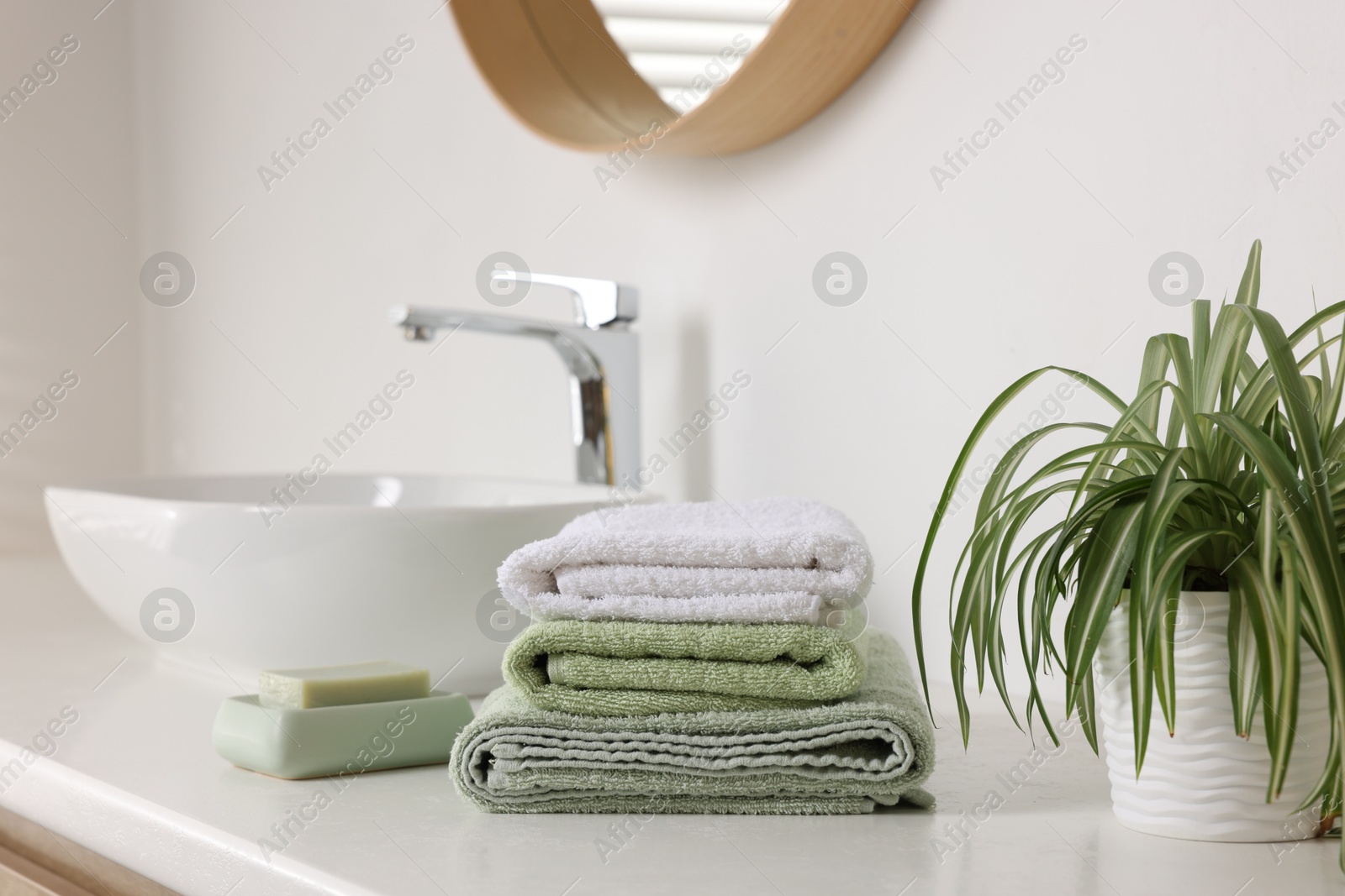 Photo of Stack of fresh terry towels, soap and plant on counter near sink