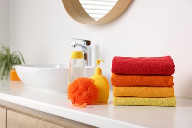 Photo of Stack of fresh terry towels, cosmetic products and sponge on counter near sink