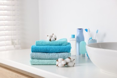 Photo of Stack of fresh terry towels and cotton flowers on counter near sink