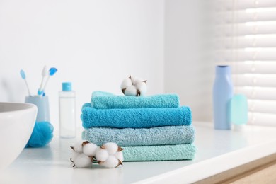 Photo of Stack of fresh terry towels and cotton flowers on counter near sink