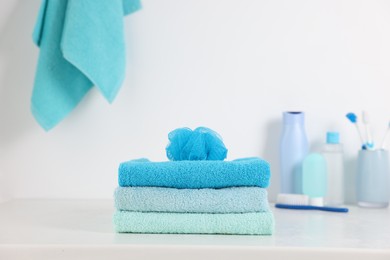 Photo of Stack of fresh terry towels and sponge on white table in bathroom