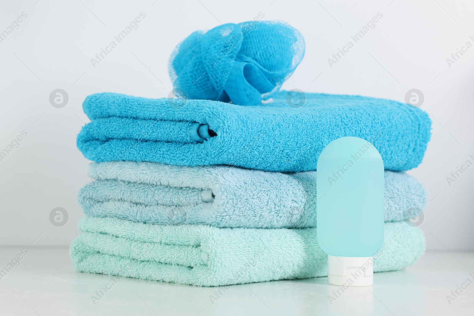 Photo of Stack of fresh terry towels, cosmetic product and sponge on white table in bathroom, closeup