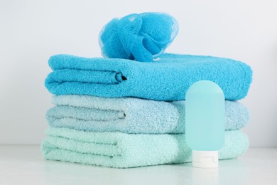 Photo of Stack of fresh terry towels, cosmetic product and sponge on white table in bathroom, closeup