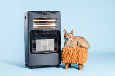 Photo of Cute little dog on pouf near electric heater against light blue background