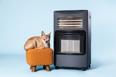 Photo of Cute little dog on pouf near electric heater against light blue background