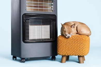 Photo of Cute little dog on pouf near electric heater against light blue background