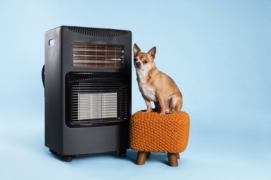 Photo of Cute little dog on pouf near electric heater against light blue background
