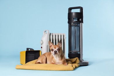 Photo of Cute little dog on blanket near electric heaters against light blue background