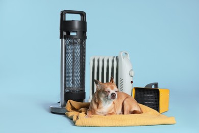 Photo of Cute little dog on blanket near electric heaters against light blue background
