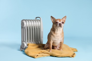 Photo of Cute little dog on blanket near electric heater against light blue background