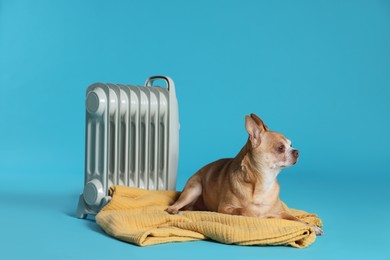 Photo of Cute little dog on blanket near electric heater against light blue background