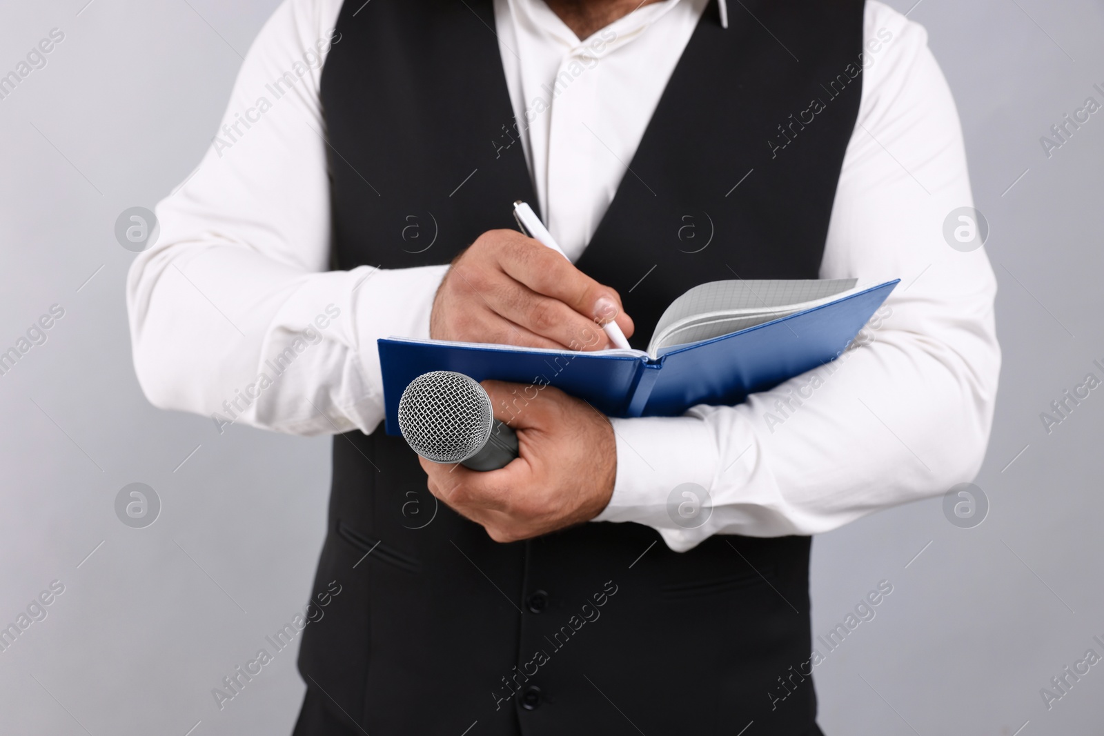 Photo of Journalist with microphone taking notes on light background, closeup