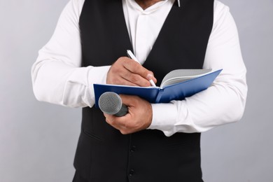 Photo of Journalist with microphone taking notes on light background, closeup