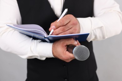 Photo of Journalist with microphone taking notes on light background, closeup