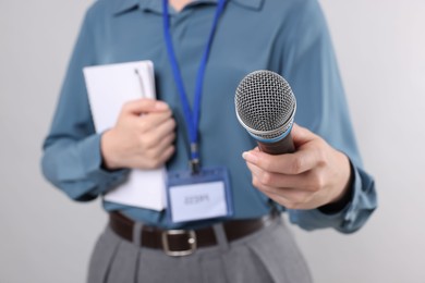 Photo of Journalist with microphone, notebook and pen on light background, closeup