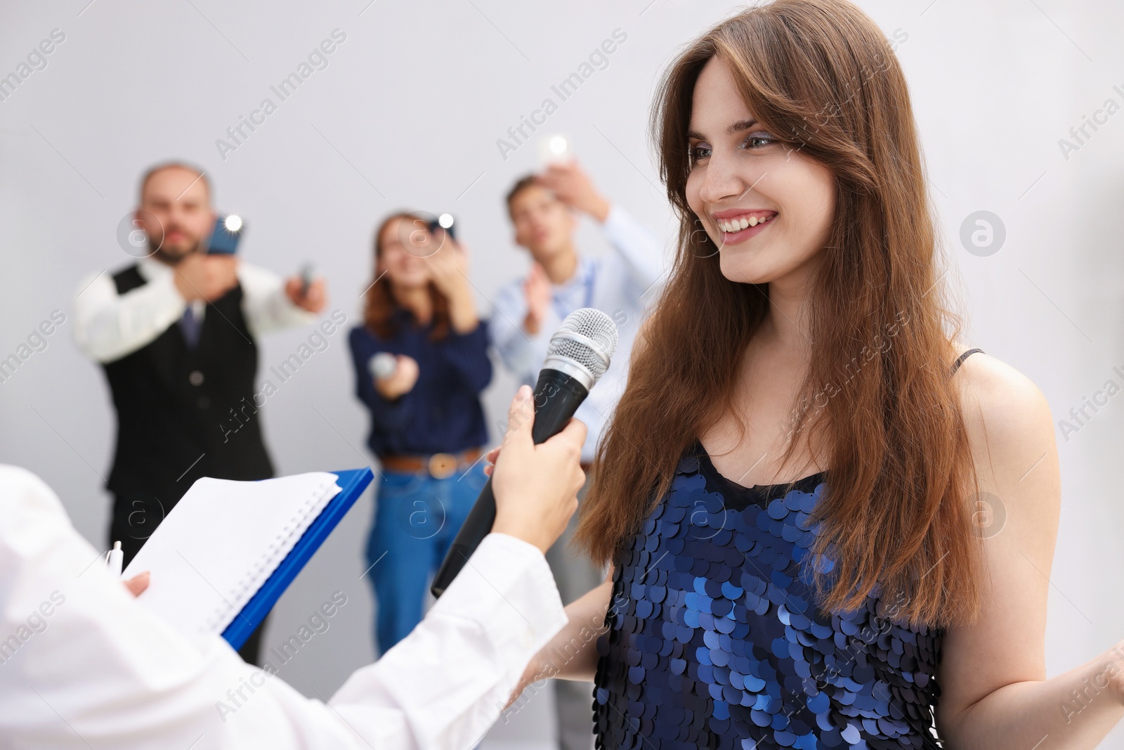Photo of Beautiful woman giving interview to journalists on light background