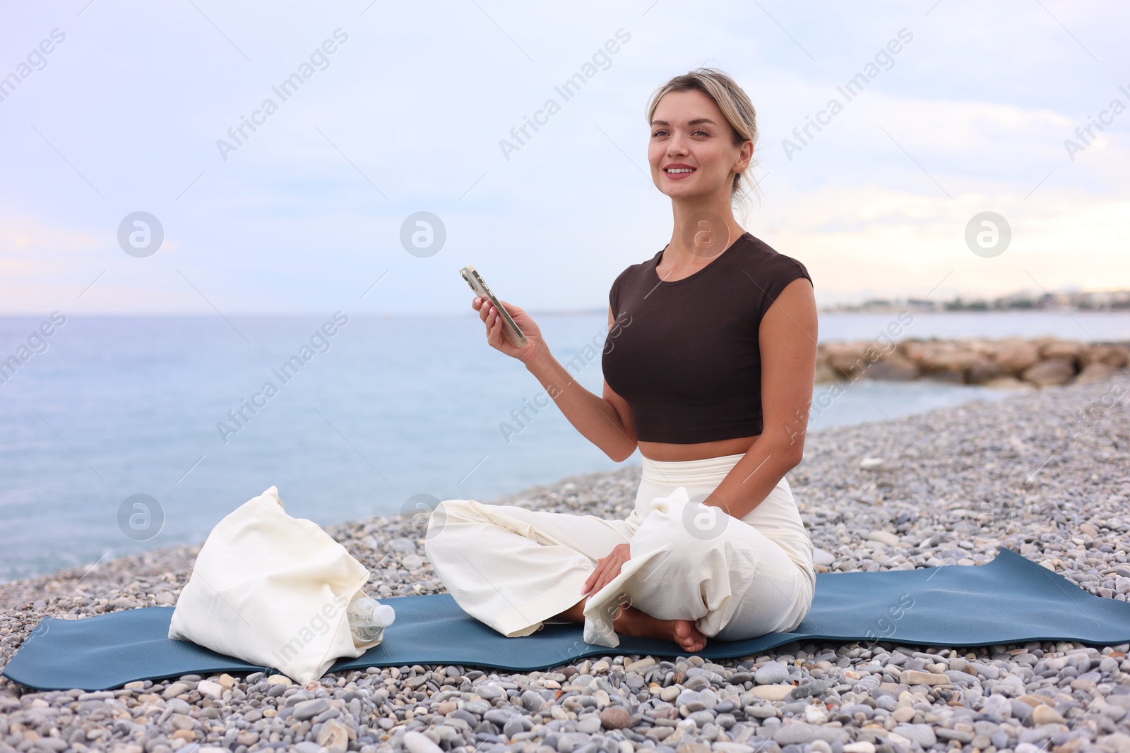 Photo of Young woman with phone on mat at beach