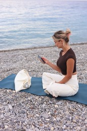 Photo of Young woman with phone on mat at beach