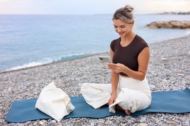Photo of Young woman with phone on mat at beach