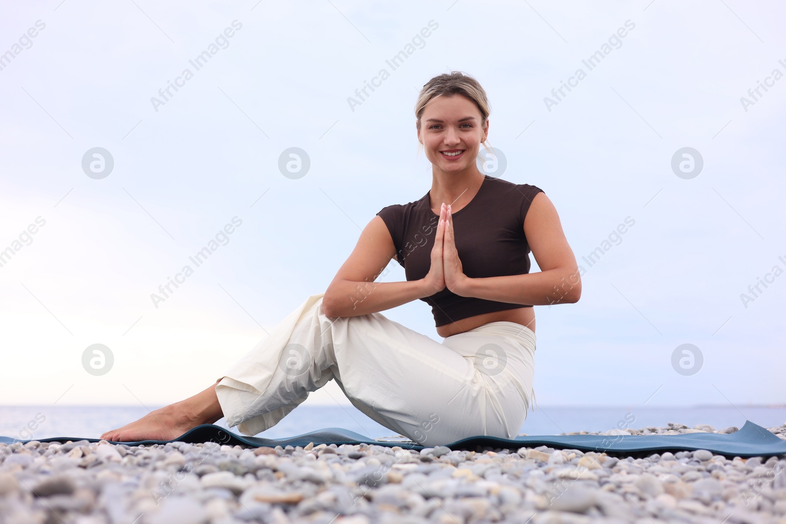 Photo of Young woman practicing yoga on mat at beach