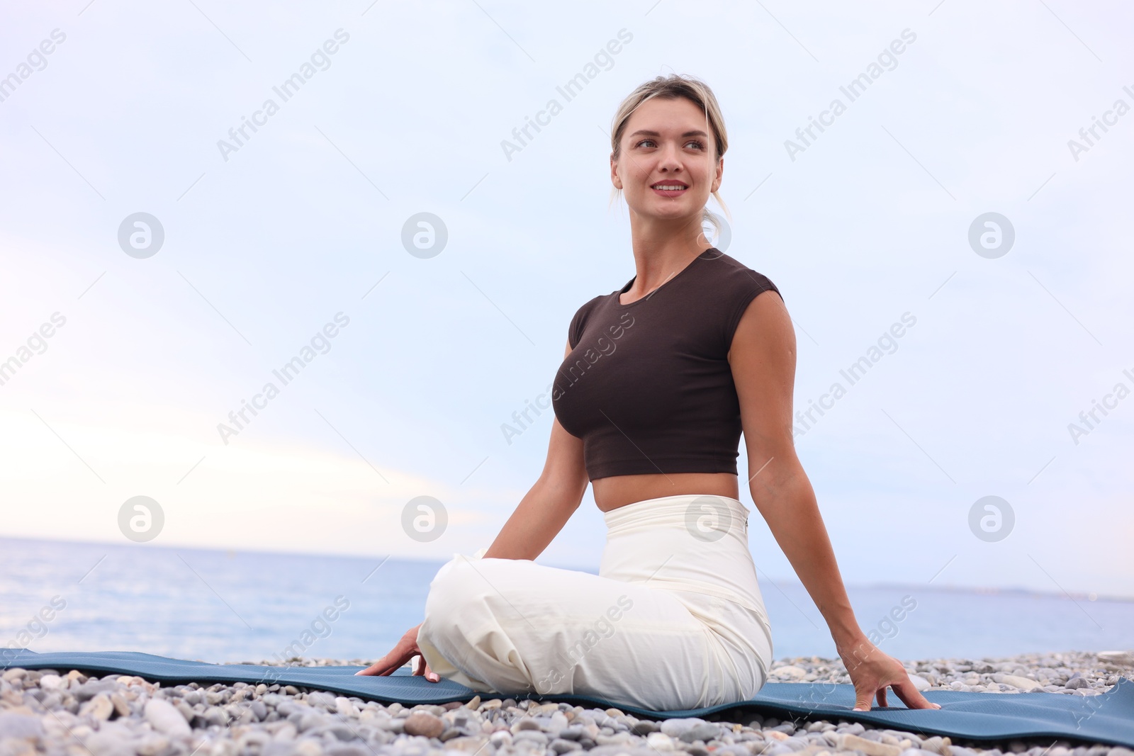 Photo of Young woman practicing yoga on mat at beach, space for text