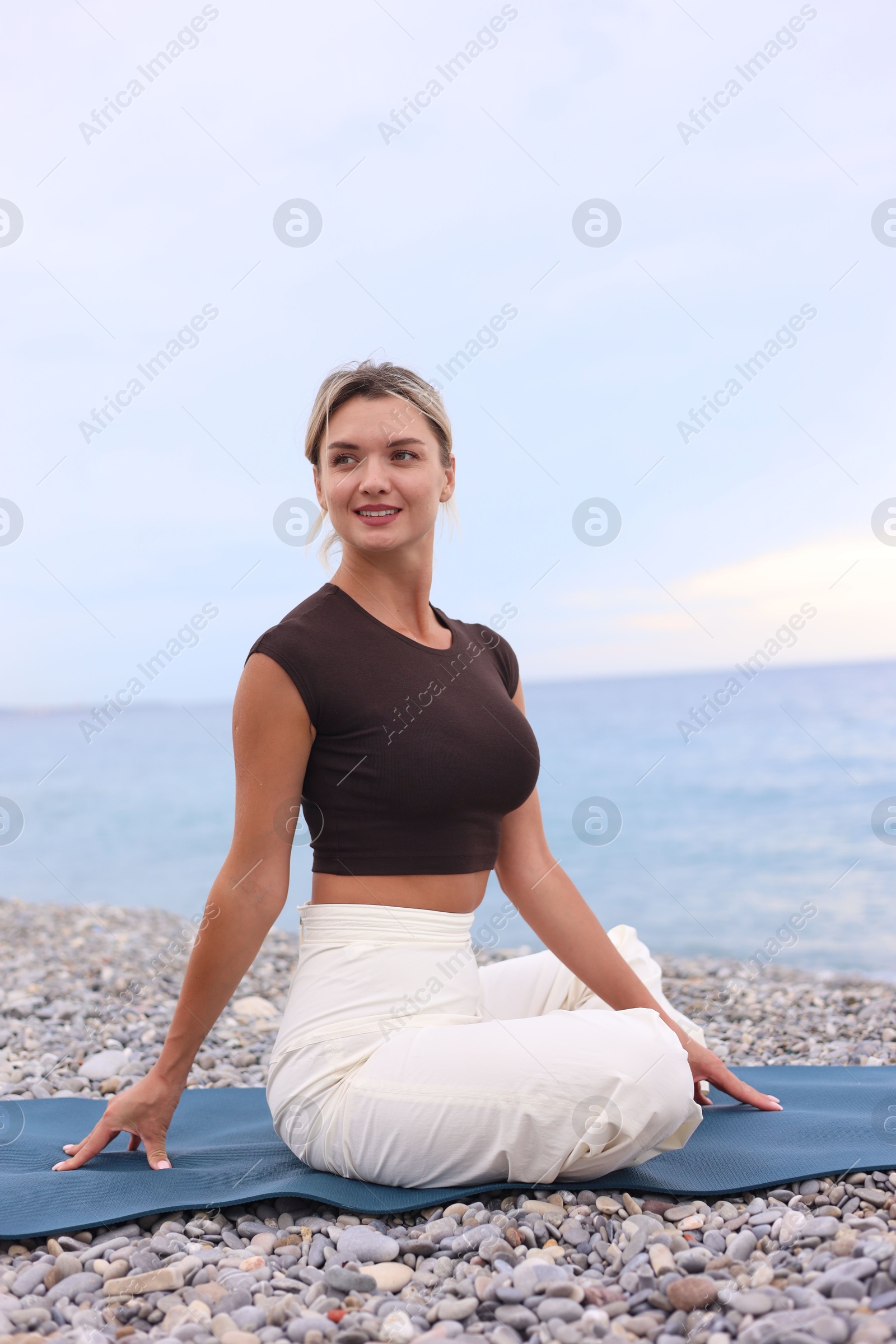 Photo of Young woman practicing yoga on mat at beach