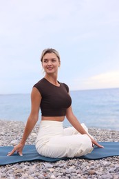 Photo of Young woman practicing yoga on mat at beach