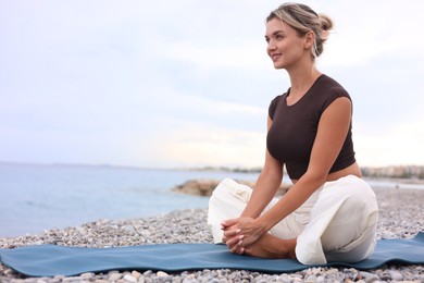 Photo of Young woman practicing yoga on mat at beach, space for text