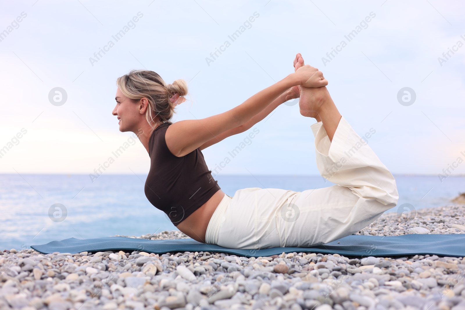 Photo of Young woman practicing yoga on mat at beach