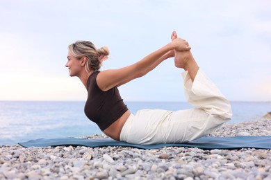 Photo of Young woman practicing yoga on mat at beach