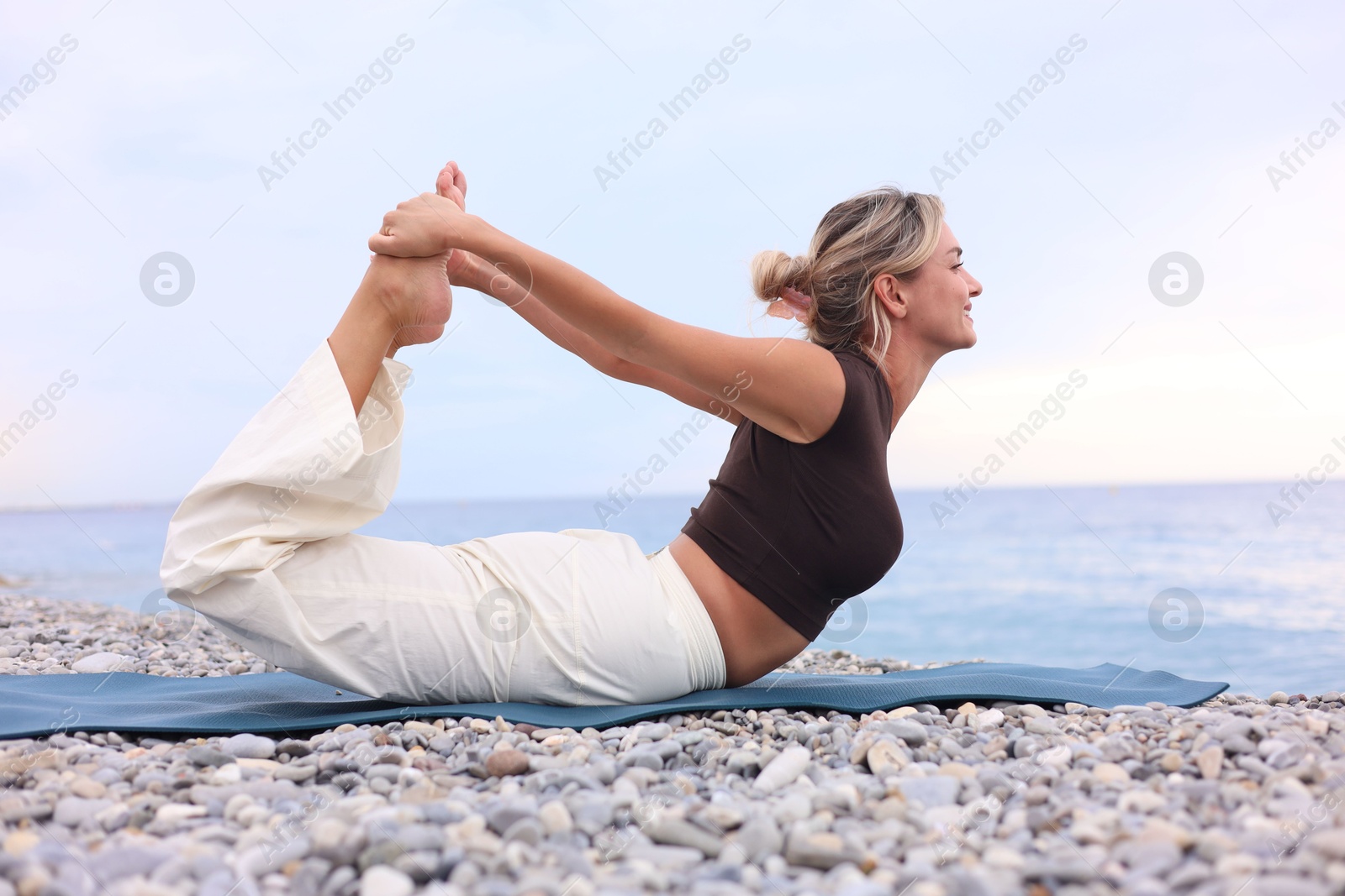 Photo of Young woman practicing yoga on mat at beach