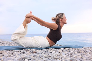 Photo of Young woman practicing yoga on mat at beach