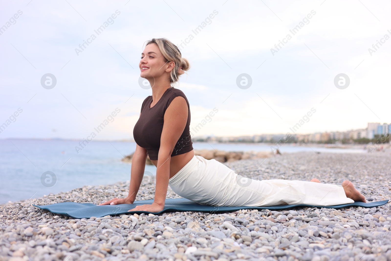 Photo of Young woman practicing yoga on mat at beach