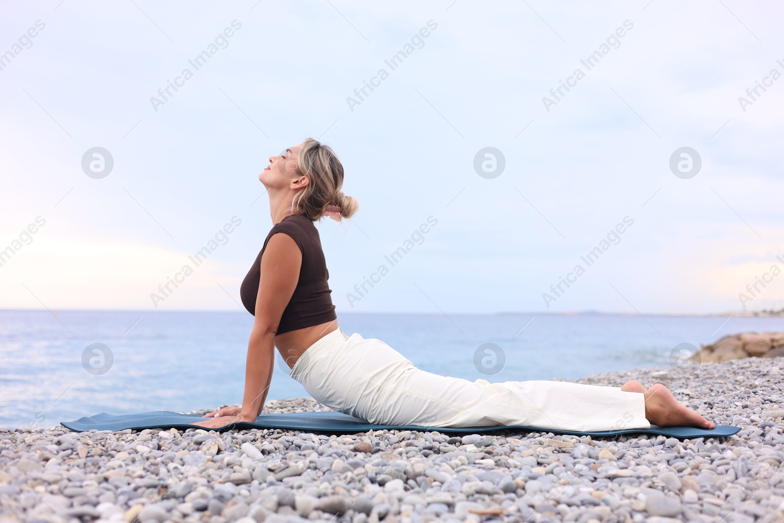Photo of Young woman practicing yoga on mat at beach