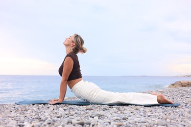 Photo of Young woman practicing yoga on mat at beach