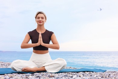 Photo of Young woman practicing yoga on mat at beach, space for text