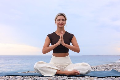 Photo of Young woman practicing yoga on mat at beach